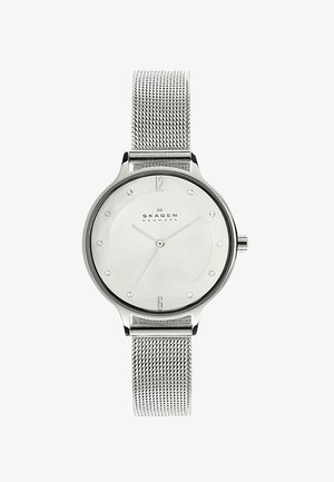 Montre Skagen argentée avec un bracelet en mesh, cadran rond minimaliste, fond blanc, index des heures argentés et cristaux subtils aux positions 3, 6, 9 et 12.