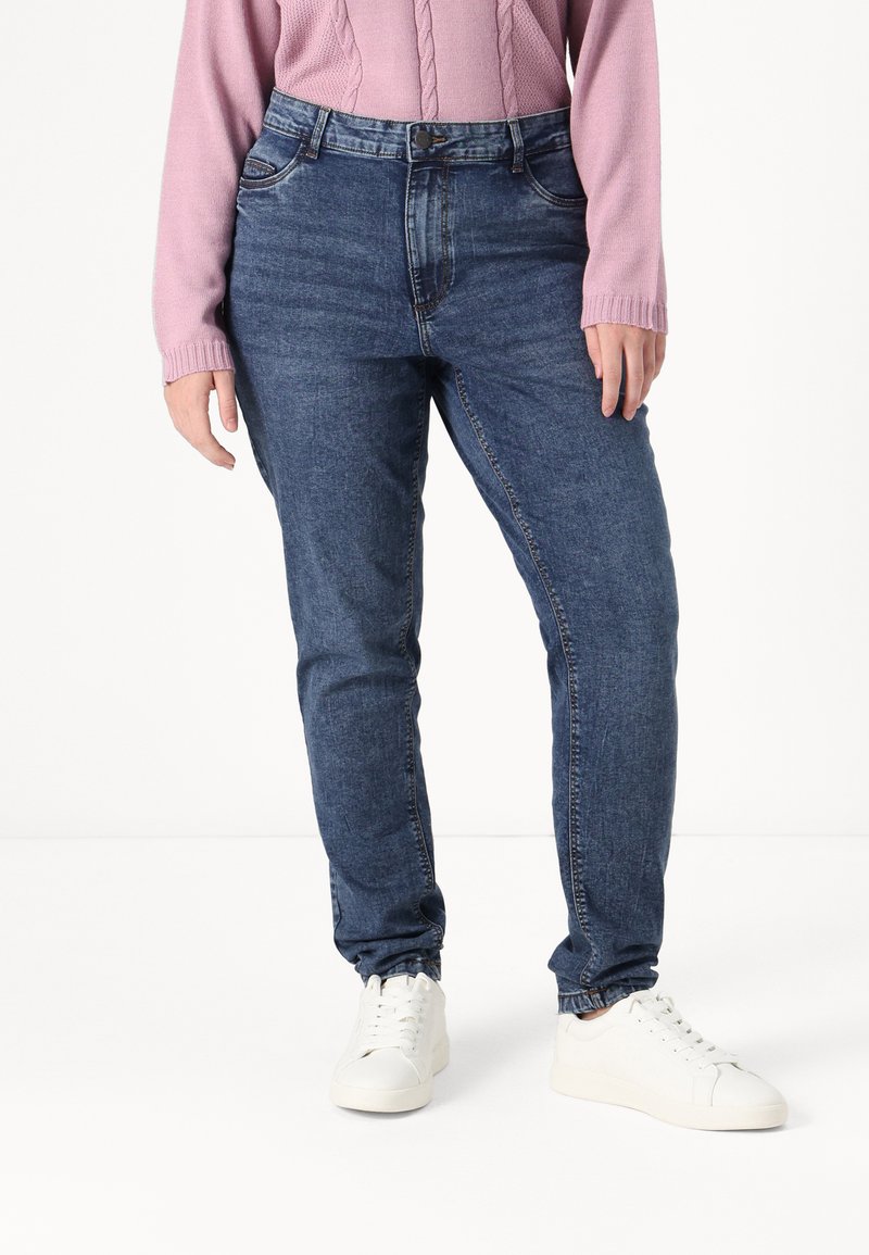 Blue denim jeans with a slim fit, featuring a classic five-pocket design and a mid-rise waist. Worn with a pink knit sweater and white sneakers.