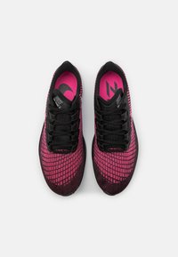 Schwarze und rosa Sportschuhe mit einem strukturierten Mesh-Obermaterial, das ein Gittermuster aufweist, schwarzen Schnürsenkeln und einer gepolsterten Innensohle.