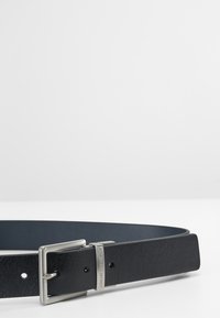 Cintura nera in pelle con una fibbia rettangolare in tonalità argento con incisione del marchio, texture liscia e numerosi fori per la regolazione.