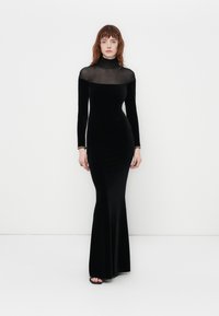 Black velvet long-sleeve gown with a sheer neck and upper bodice. Fitted silhouette flares at the bottom. Simple silver bracelet accents.