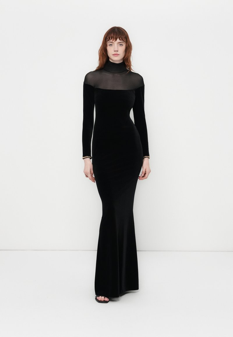 Black velvet long-sleeve gown with a sheer neck and upper bodice. Fitted silhouette flares at the bottom. Simple silver bracelet accents.