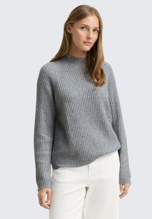 Pull gris à côtes avec un col montant et des manches longues, fabriqué en matériau texturé, associé à un pantalon de couleur claire.