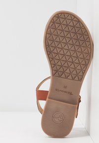 Semelle de sandale en cuir fauve avec une semelle en caoutchouc texturée, présentant un motif géométrique et un logo embossé. Taille indiquée : 37.