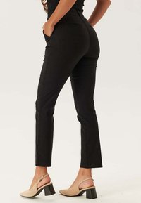 Svarta slim-fit byxor med fickor och textilerat material. Har hög midja och rak ben-design, i kombination med beige klacksandaler.
