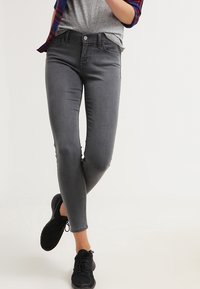 Jeans gris de corte slim con una textura suave y un diseño clásico de cinco bolsillos, combinados con zapatillas deportivas negras, creando un look casual.