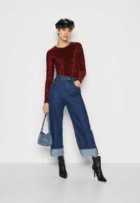 Czerwony longsleeve z falistym wzorem, niebieskie dżinsy typu wide-leg z wysokim stanem, czarne botki na kostkę i czapka w kolorze czarnym. Mała torebka dżinsowa.