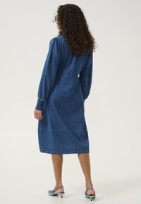 Jeansklänning med långa ärmar, figurnära liv och A-linjeformad silhuett. Har samlade ärmar, lagerkjol och en mörkblå nyans.