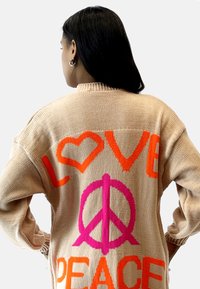 Maglione lavorato a maglia beige con grandi simboli arancioni "LOVE" e rosa "PEACE" sulla schiena, con un design a cuore e simbolo della pace.