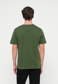 Πράσινο κοντομάνικο μπλ�ουζάκι με στρογγυλή λαιμόκοψη, φτιαγμένο από μαλακό ύφασμα, απλή υφή και λιτό σχέδιο, εμφανίζεται από πίσω.