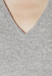 Pull en tricot gris avec un design en V. Texture douce et motif subtil visible, mettant l'accent sur la zone du col.