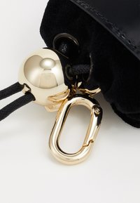 Sac en tissu noir avec une cloche dorée brillante et un clip carabine doré, présentant une surface texturée et un détail de fermeture à cordon.