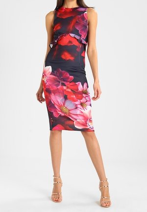 Femme portant une robe sans manches jusqu'aux genoux avec un grand imprimé floral rouge et rose et un détail à volants à la taille, associée à des talons à brides.