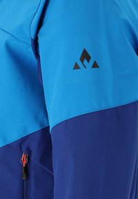 Blå och lila utomhusjacka med kvartslång dragkedja, slät textur och en svart logotyp på axeln.