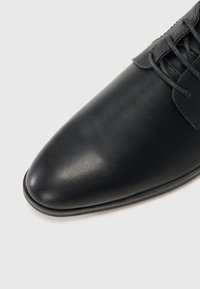 Zapato de cuero negro con un acabado suave, punta afilada y cordones a tono. Presenta un ligero brillo y una suela delgada de goma.