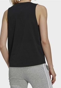 Svart ärmlös tanktop med en avslappnad passform, med en slät textur och rundad halsringning, kombinerad med grå träningsbyxor.