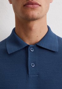 Blauwe poloshirt van een gestructureerde stof, met een klassieke kraag, een placket met drie knopen en een effen kleur zonder extra patronen.