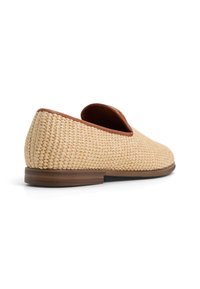 Woven beige shoes with a smooth brown leather accent at the heel, featuring a low profile design and flat brown sole.