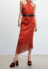 Vestido de satén rojo de tirantes con patrón floral texturizado, dobladillo con flecos, cintura ceñida, combinado con un cinturón negro y zapatos de plataforma burdeos.