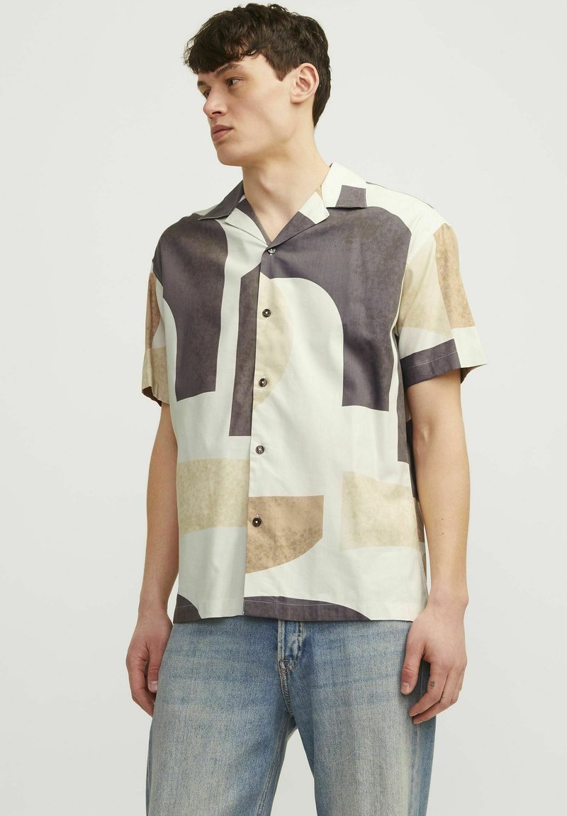 Chemise à manches courtes en tissu tissé, ornée d'un motif géométrique abstrait dans des teintes crème, beige et gris foncé. Fermeture à six boutons sur le devant.