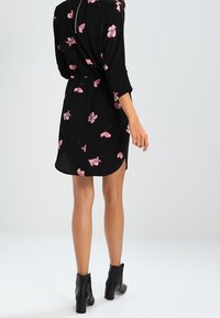 Vestido negro con flores rosas, cinturilla con cinturón, mangas de tres cuartos y dobladillo redondeado. Combinado con botas negras hasta el tobillo.