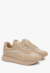 Beige sneakers met een mix van suède en mesh materialen. Beschikt over een gestructureerde zool, vetersluiting en opvallende zijpanelen van mesh.