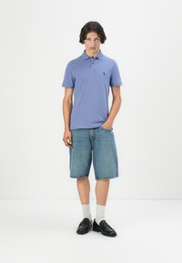 Svetle fialové polo tričko s krátkým rukávem, spárované s džínovými šortkami do kolen. Černé boty a bílé ponožky doplňují celý outfit.
