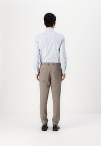 Lys blåstripet skjorte, middels passform, med lange ermer. Beige bukser i avslappet snitt, med to baklommer. Sorte sko.