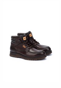 Bottines en cuir marron avec une finition lisse, un col rembourré et une semelle en caoutchouc. Présente des œillets noirs et un logo de marque orange sur la languette.