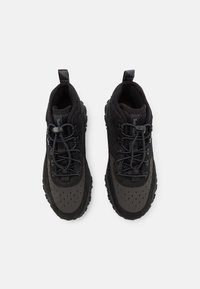 Czarne buty sportowe z teksturowaną siateczkową cholewką, wzmocnionym czubkiem, wiązane na sznurówki i posiadające wyraźną gumową podeszwę z przyczepnością.