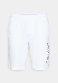 Short blanc longueur genou avec taille élastique et logo Calvin Klein vertical noir sur la jambe droite.