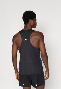 Μαύρη αθλητική μπλούζα με ριγέ υφή, σχέδιο racerback και ανακλαστική λεπτομέρεια στην πλάτη. Συνδυασμένη με μαύρες βερμούδες.