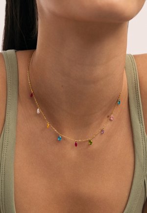 Delicado collar de cadena de oro con pequeñas gemas multicolores en forma de lágrima, llevado en el cuello de una persona con una camiseta sin mangas verde oliva.