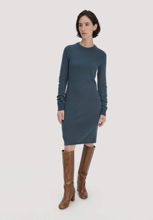 Dunkelblaumes Strickkleid mit langen Ärmeln und Rundhalsausschnitt, kombiniert mit braunen, knielangen Stiefeln mit Absatz. Glatte Textur im gesamten Kleid.