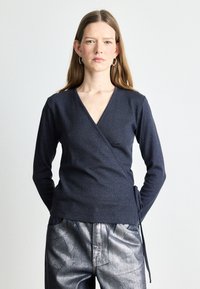 Granatowy sweter w stylu kopertowym z długimi rękawami, teksturowana tkanina i zawiązania z boku, w zestawieniu ze srebrnymi, szerokimi spodniami.