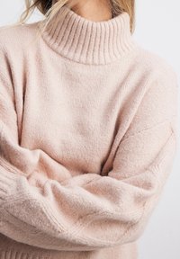 Ljusrosa polotröja med ribbad halsringning och ärmslut, tillverkad av mjukt, texturerat stickmaterial och med en avslappnad passform.