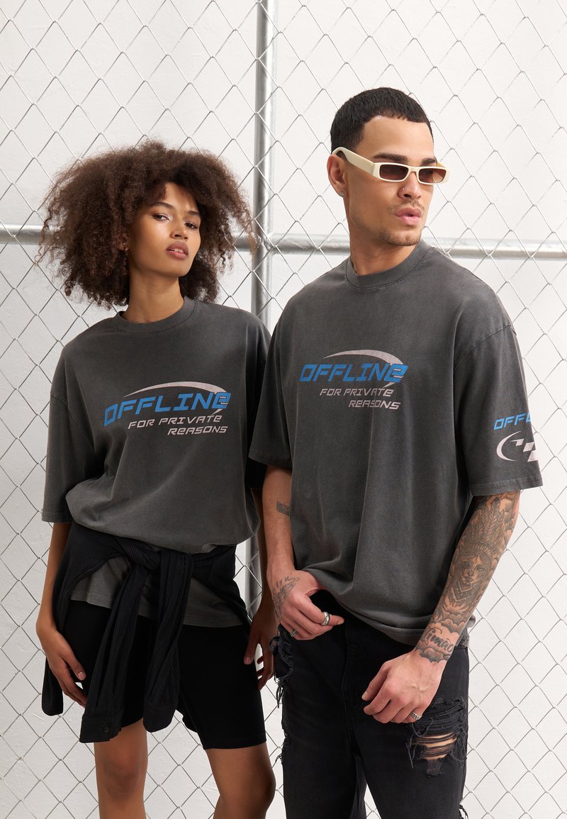 Grå oversized t-shirts med "OFFLINE FOR PRIVATE REASONS" print i blå. Casual pasform, korte ærmer, båret med sorte shorts og jeans.