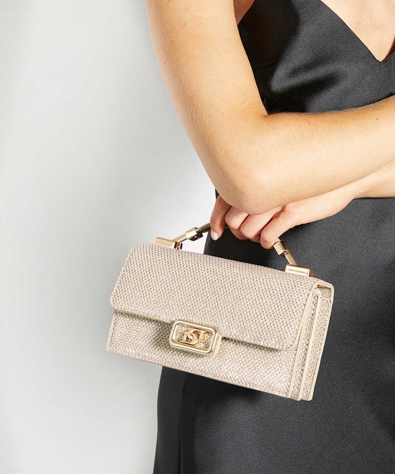 Femme en robe noire tenant un sac à main beige texturé avec un fermoir doré et une poignée sur un fond clair uni.