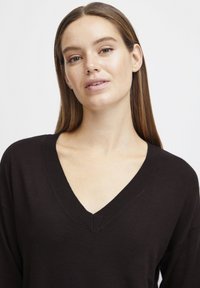 Schwarzer V-Ausschnitt-Pullover mit langen Ärmeln, geripptem Ausschnitt und lockerer Passform, gefertigt aus weichem, leichtem Strickstoff.