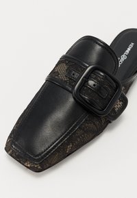 Mule en cuir noir avec bout carré, overlay en dentelle et grande bride noir à boucle sur le dessus, semelle intérieure griffée visible.