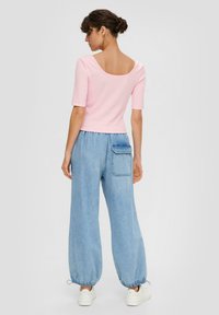 Różowa, dopasowana bluzka z krótkim rękawem i szerokim dekoltem, w zestawie z luźnymi, jasnoniebieskimi dżinsami posiadającymi elastyczny mankiet i tylną kieszeń.