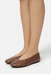 Bruine leren ballerina's met een ronde neus, voorzien van metalen studs die gelijkmatig over het oppervlak zijn verspreid. De schoenen hebben een lage profiel en een platte zool.