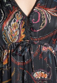 Musta mekko värikkäillä kukkakuvioilla, V-pääntie, pitsin reunus ja säädettävä vyötärösolki. Rakenteellinen kangas, jossa on pystysuorat raidat.