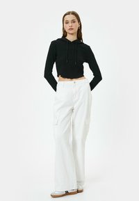 Sudadera recortada negra con mangas largas y parte inferior en forma de ondas, combinada con pantalones cargo blancos que cuentan con bolsillos laterales y un corte holgado.