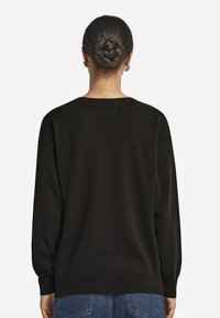 Brauner Strickpullover mit lässiger Passform, Rundhalsausschnitt und langen Ärmeln. Verfügt über eine weiche Textur und gerippte Säume. Getragen mit blauen Jeans.