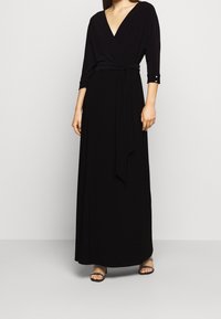 Vestido negro de manga larga con envoltura, escote en V profundo y cintura ajustada, con una falda fluida y un cinturón de lazo. Tejido liso y sólido.