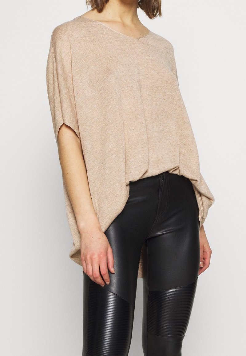 Beżowy, oversize sweter z krótkimi rękawami, wykonany z miękkiego materiału. Połączony z czarnymi legginsami z sztucznej skóry, zdobionymi detalami z żebrowanego materiału.