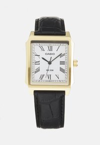 Montre carrée Casio avec un boîtier doré, un cadran blanc, des chiffres romains, un bracelet en cuir noir et une étanchéité de 50 mètres.