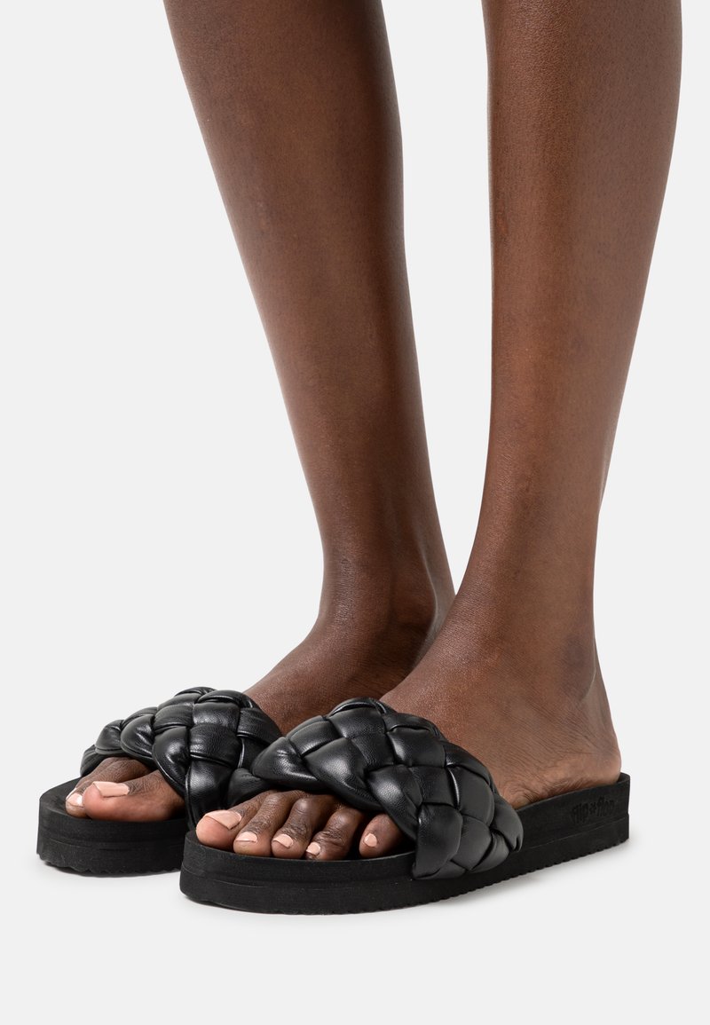 Black woven slide sandals feature thick braided straps and a textured rubber sole. Designed for slip-on wear, they are open-toed and minimalist.