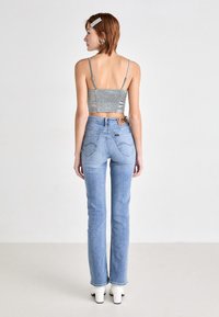 Top corto argento con retro arricciato, abbinato a jeans svasati azzurri chiari con una patch del logo e cuciture delicate sulle tasche posteriori.